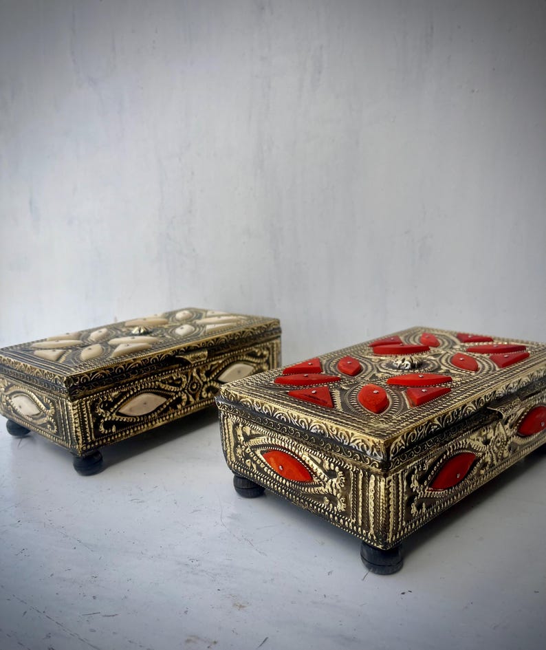 May include: Two ornate decorative boxes with intricate designs. One box is gold with red accents and the other is gold with white accents.