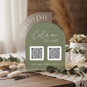 May include: An arched acrylic payment sign featuring a sage green background with white text that reads scan to pay, Color me BY AMY, and TIPS ARE APPRECIATED. The sign includes two white square QR code icons centered on the green surface.