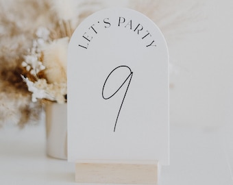 May include: White table number card with an arch shape and the text "Let's Party" in a black script font. The number "9" is written in a black script font in the center of the card.