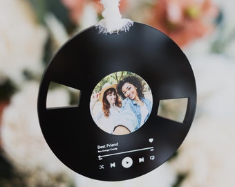 May include: Black round ornament with a photo of two women smiling. The ornament has a music player design with the words "Best Friend" and a heart icon.