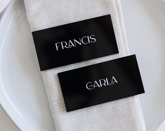 May include: Two black place cards with white text. The top card reads "FRANCIS" and the bottom card reads "CARLA".