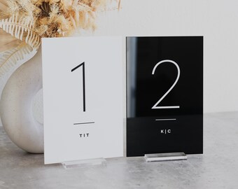 May include: Two acrylic table numbers, one white with black text and the number "1" and the text "TIT", and one black with white text and the number "2" and the text "K|C".