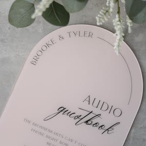 May include: A pink, arched sign with the words "Brooke & Tyler" at the top. Below, it reads "Audio Guestbook" in elegant script. The sign provides instructions for leaving a message.