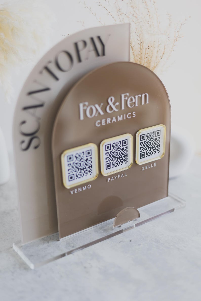 May include: A clear acrylic stand with a brown arched sign that says "Fox & Fern Ceramics." The sign has three QR codes for Venmo, PayPal, and Zelle. The words "SCAN TO PAY" are on a curved panel.