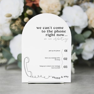 May include: White sign with a black outline of a phone and the text "we can't come to the phone right now... we are celebrating!"  The sign also has instructions for leaving a message: "pick up the phone 01", "leave us a message after the beep 02", and "hang up to ensure your message was recorded! 03". The sign is signed "Phillip & Amy".