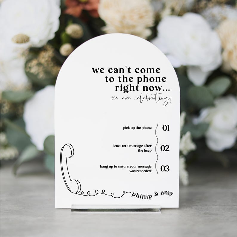 May include: White sign with a black outline of a phone and the text "we can't come to the phone right now... we are celebrating!"  The sign also has instructions for leaving a message: "pick up the phone 01", "leave us a message after the beep 02", and "hang up to ensure your message was recorded! 03". The sign is signed "Phillip & Amy".