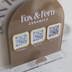 May include: A brown acrylic payment display for Fox & Fern Ceramics, with QR codes for Venmo, PayPal, and Zelle. The display has a clear base and a curved top with the brand name in white lettering.