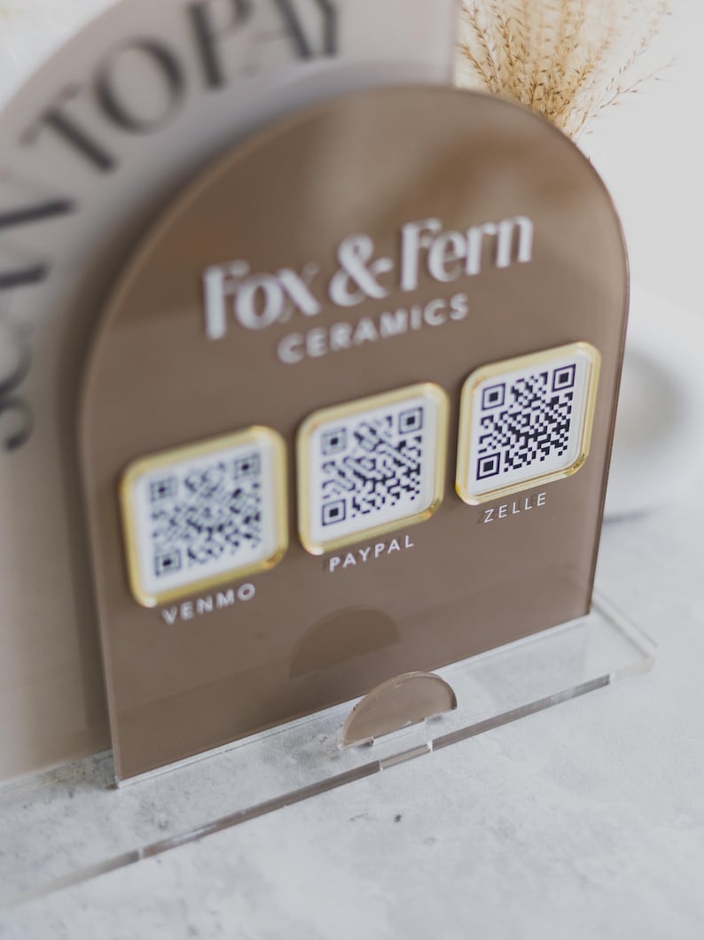 May include: A brown acrylic payment display for Fox & Fern Ceramics, with QR codes for Venmo, PayPal, and Zelle. The display has a clear base and a curved top with the brand name in white lettering.