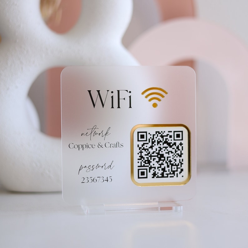 May include: A clear acrylic WiFi sign with gold accents. The sign displays the word "WiFi" and a WiFi symbol, along with the network name "Coppice & Crafts", a password, and a QR code for easy access.