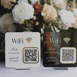 May include: Two square WiFi signs, one white and one black, with gold accents. Each sign displays "WiFi", a signal icon, a QR code, and network information. The white sign reads "Spectrum 348" and the black sign reads "That salon guest".