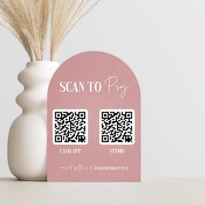 May include: A blush pink arched sign with the words "SCAN TO Pay" in white script. Below are two QR codes labeled "CASH APP" and "VENMO". A white vase with dried pampas grass is to the left.