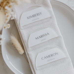 May include: Three white acrylic place cards with rounded edges and black text. The top card reads "KIMBERLY johnson", the middle card reads "MARISSA phan", and the bottom card reads "CAMERON davidson".