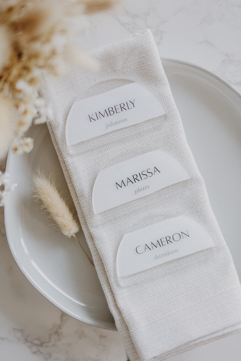 May include: Three white acrylic place cards with rounded edges and black text. The top card reads "KIMBERLY johnson", the middle card reads "MARISSA phan", and the bottom card reads "CAMERON davidson".