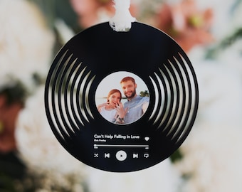 May include: Black circular ornament with a photo of a couple in the center. The ornament has a record player design with concentric circles and a music player interface at the bottom. The text "Can't Help Falling In Love" is displayed above the music player interface.