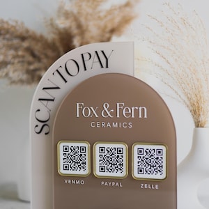 May include: A clear acrylic point-of-sale display with a tan and brown arched design. The display features the text "SCAN TO PAY" and "Fox & Fern Ceramics" with QR codes for Venmo, PayPal, and Zelle.