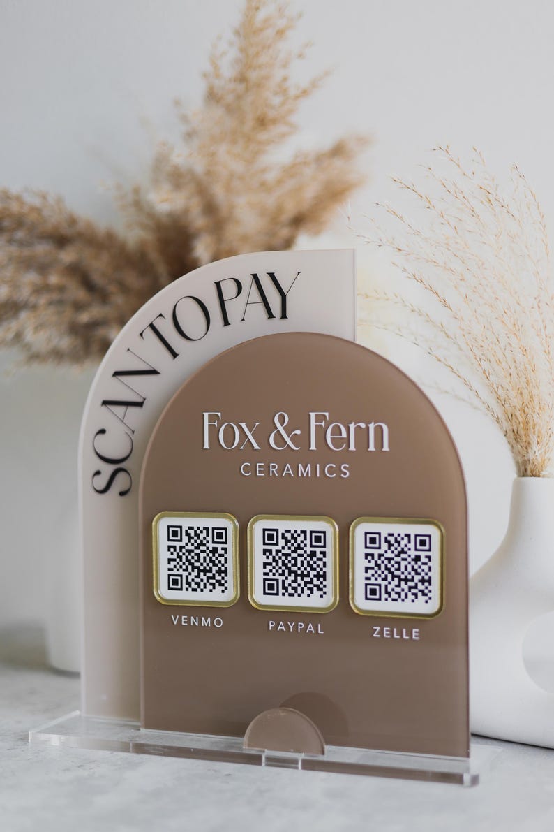May include: A clear acrylic point-of-sale display with a tan and brown arched design. The display features the text "SCAN TO PAY" and "Fox & Fern Ceramics" with QR codes for Venmo, PayPal, and Zelle.
