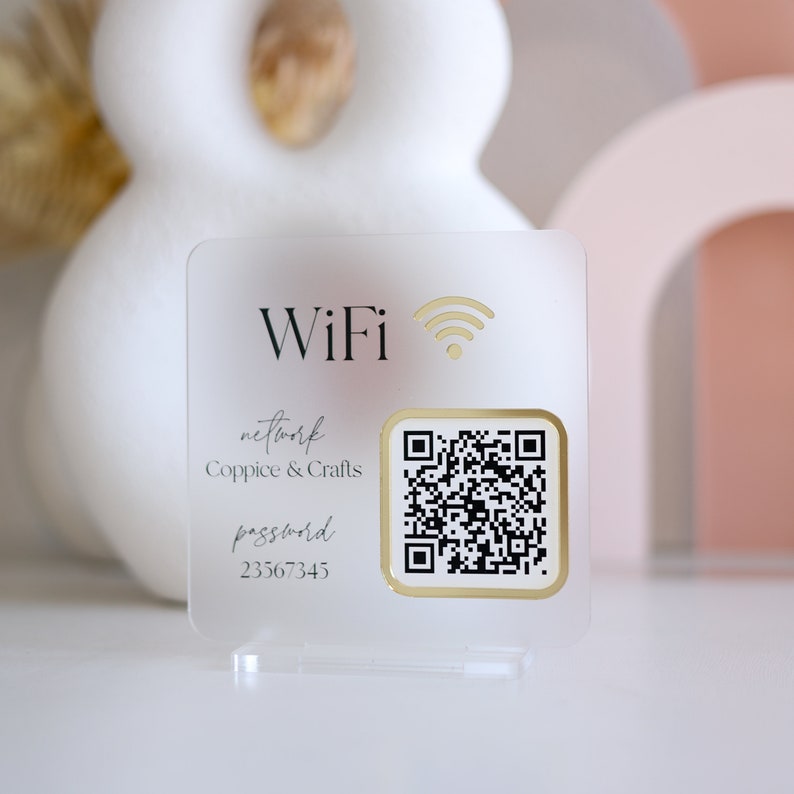 May include: A clear acrylic WiFi sign with gold accents. The sign displays the word "WiFi" and a WiFi symbol in gold. Below, it reads "network Coppice & Crafts password 23567345" and includes a QR code.