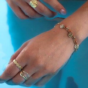 May include: A gold-toned jewelry set featuring a textured ring, a delicate ring with floral details, and a bracelet with coin-shaped charms. The jewelry is displayed against a blue background, creating a striking contrast. The pieces are designed with intricate details.