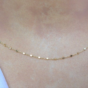 May include: A delicate gold chain necklace with small square links. The necklace is simple and elegant, perfect for everyday wear.