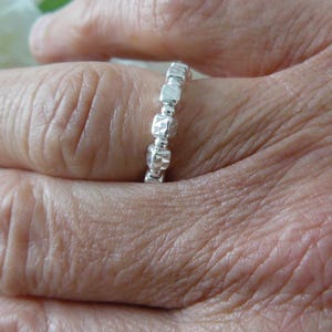 May include: A silver ring with a textured, hammered finish. The ring is made up of small, square-shaped beads.