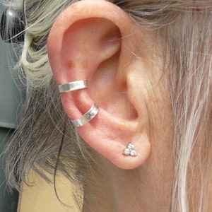Peut inclure: Une oreille avec deux boucles d'oreilles argentées et un petit piercing argenté avec trois petites pierres.