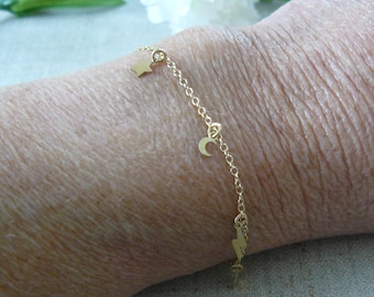 May include: A delicate gold-colored bracelet featuring a star, crescent moon, and lightning bolt charm. The bracelet is made of a fine chain and is designed to be worn on the wrist. The charms are small and add a touch of whimsy.