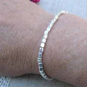 May include: A silver bracelet made of small, square-shaped beads.