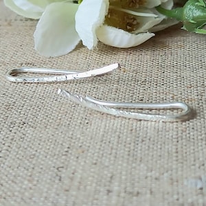 Peut inclure: Deux boucles d'oreilles argentées avec une finition texturée. Les boucles sont incurvées et ont un design simple.