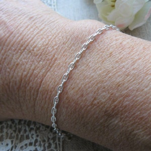 Puede incluir: Un brazalete de cadena de plata con un delicado diseño de eslabón de ancla.