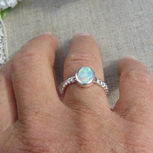 Peut inclure: Une bague en argent avec une opale blanche sertie dans un sertissage à bélière. La bande de la bague est de forme torsadée.