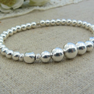 Può includere: Un braccialetto d'argento con perline e una perla d'argento più grande al centro.