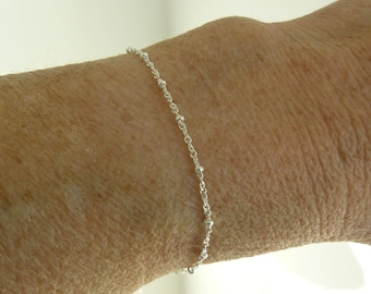 May include: A delicate silver chain bracelet with small beads. The bracelet is shown on a person's wrist.