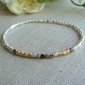 May include: A silver bracelet with gold and black beads. The bracelet is made of small square beads.