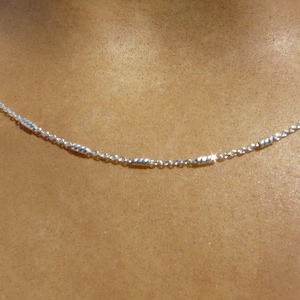 Peut inclure: Un collier en chaîne argent avec de petites perles cylindriques texturées.
