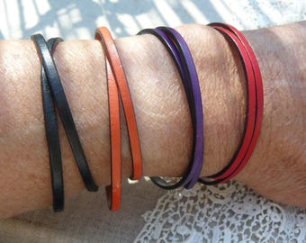 May include: A collection of thin leather bracelets in various colors, including black, orange, purple, and red. The bracelets are wrapped around a wrist, showcasing their simple, minimalist design. The bracelets are a stylish accessory.