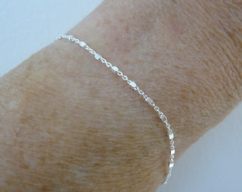 May include: A silver chain bracelet with a delicate, linked design. The bracelet is shown on a person's wrist.
