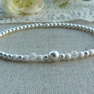 Peut inclure: Un bracelet en argent composé de perles, avec une perle centrale texturée et deux perles décoratives de chaque côté.
