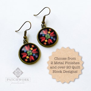 May include: A pair of round earrings with a bronze finish. Each earring features a colorful quilt block design on a black background. The earrings have a hook closure. The image also includes text that says "Choose from 2 Metal Finishes and over 20 Quilt Block Designs!"