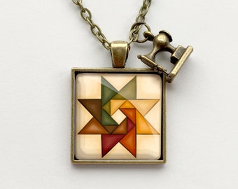 May include: A gold necklace with a square pendant featuring a colorful geometric star design. The pendant is surrounded by a bronze frame. A small sewing machine charm hangs from the necklace.