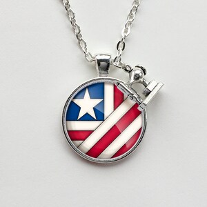 May include: A silver necklace with a round pendant featuring a red, white, and blue American flag design. The pendant is attached to a silver chain.
