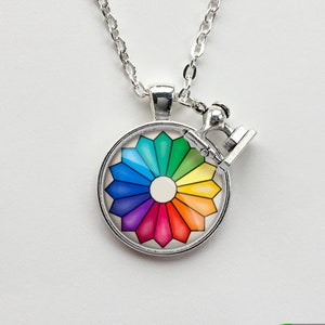 May include: A silver necklace with a round pendant featuring a colorful color wheel and a small silver sewing machine charm.