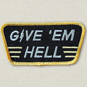 May include: A black and yellow embroidered patch with the text "GIVE 'EM HELL" in white lettering.