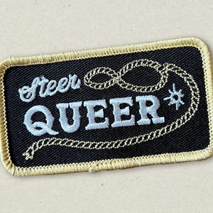 May include: Black embroidered patch with a gold chain design and the text "Steer Queer" in white.