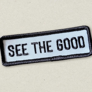 May include: White embroidered patch with black stitching and the text "SEE THE GOOD" in black.