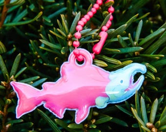 May include: A pink salmon keychain with a blue and green fish design. The keychain is attached to a pink beaded chain.