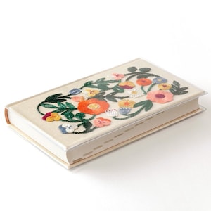 Può includere: Un libro beige con un ricamo floreale nei toni dell'arancione, rosa, giallo e blu, con foglie verdi. Il libro ha una copertina in PVC trasparente. Il testo "PVC cover" è in giapponese.
