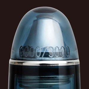 May include: Close-up of a blue pen cap with a silver band and the number "0000/3000" engraved on the cap.