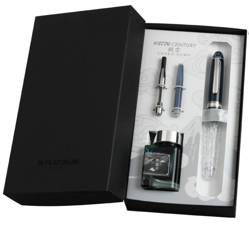 May include: A black box with a Platinum #3776 Century Urushi-Gumo fountain pen, a converter, a cartridge, and a bottle of ink. The pen has a clear, textured barrel and a silver trim. The ink bottle is clear with a green liquid and a mountain scene on the label.