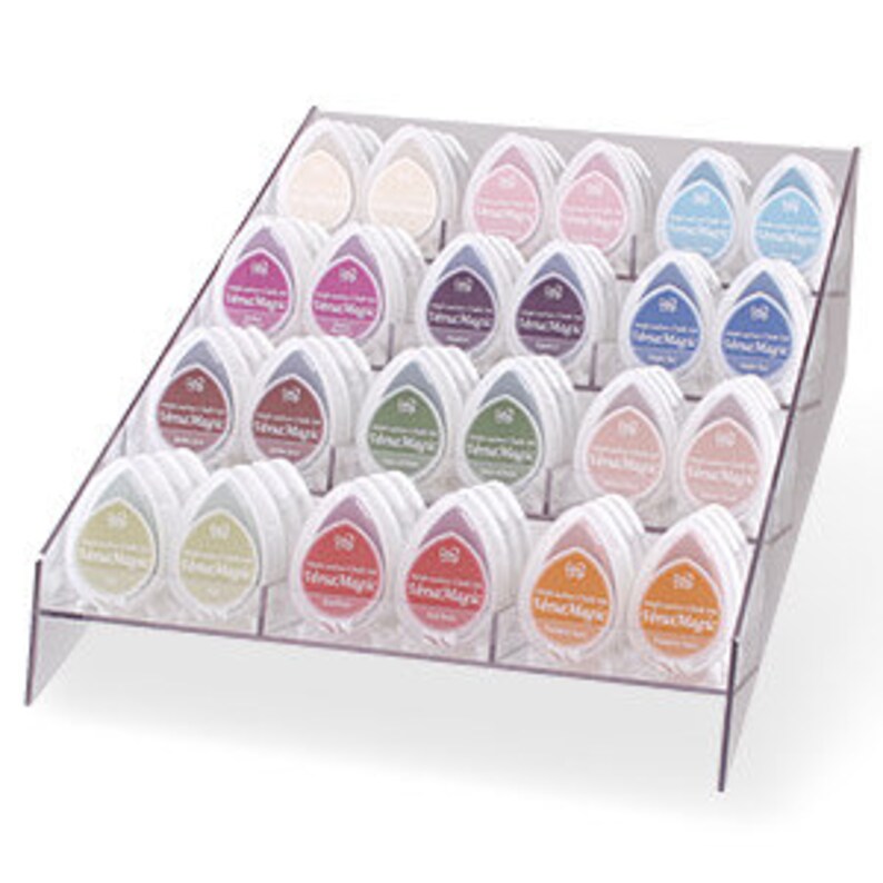May include: A clear acrylic display stand with 36 small ink pads in various colors. The ink pads are arranged in rows and are labeled "Tsukineko" and "VersaMagic".