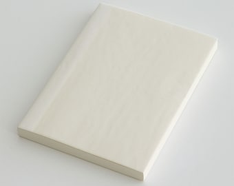 May include: A blank, off-white notebook with a soft, textured cover. The notebook is closed and lying flat on a white surface.